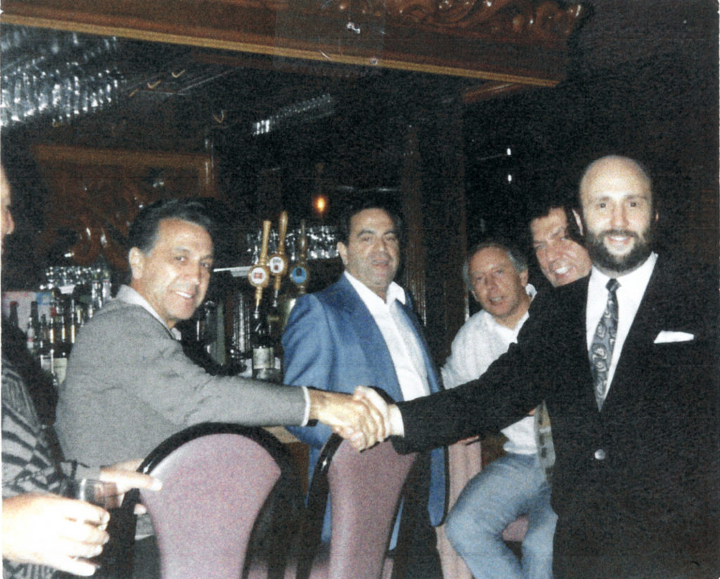 In a photo seized during a 1988 raid, mob boss John DiFronzo (far left) is seen shaking hands with a restaurateur. Marco D'Amico can just be seen peeking over the owner's shoulder.